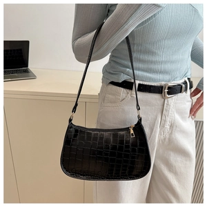 Detail of black crocodile texture shoulder bag worn by model in an indoor setting