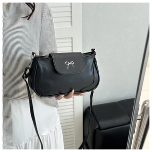 Close-up of a black leather crossbody bag with a silver bow clasp on a white door backdrop
