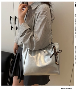 Silver metallic tote bag with wrinkled texture, bow charm, and silk scarf on chain strap