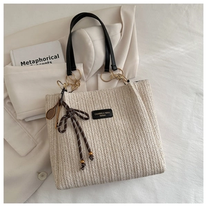 Detail of woven beige tote bag with black handles, gold rings and tennis racket charm
