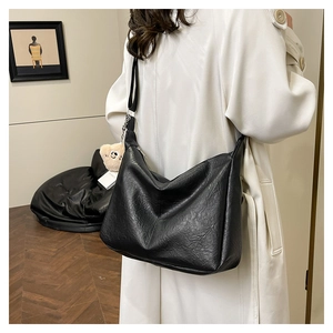 Detail of a large black hobo tote bag in oil wax leather with a cute bear charm accessory
