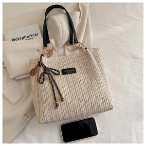 Detailed woven straw tote bag with black leather handles and tennis racket charm accessory