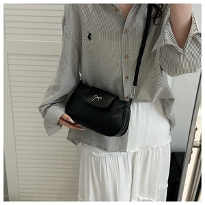 Detail of a black leather crossbody bag with a delicate silver bow metal buckle