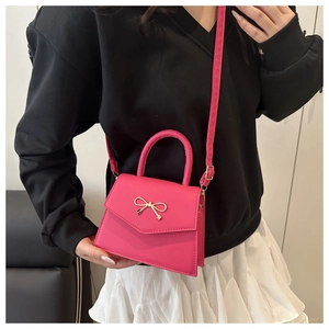 Detailed view of rose red mini handbag with golden bow metal decor and sleek PU finish