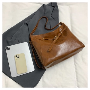 Top view of a caramel brown leather tote bag with gold hardware on a grey suit jacket