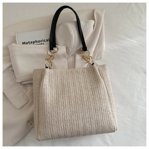 Detail of woven straw tote bag with black leather handle and golden chain link