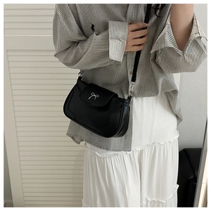 Detail of a black crossbody bag featuring a silver metal bow accent and slim strap