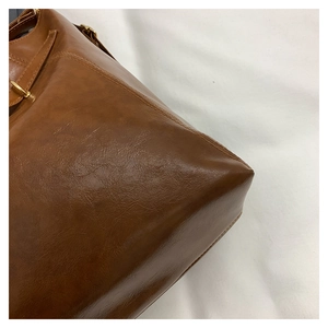 Detailed close-up of stitching and metal buckles on brown leather vintage tote bag
