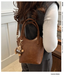 Brown faux leather tote bag with unique plush monster charm and adjustable strap detail