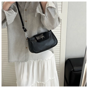 Detail of a black half-moon shoulder bag with a silver metal bow and adjustable strap