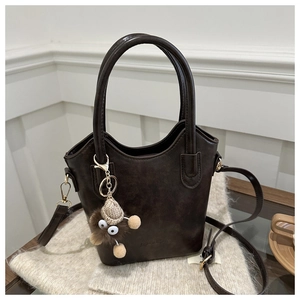 Detail of dark brown bucket bag with plush charm and soft faux leather texture on knitwear