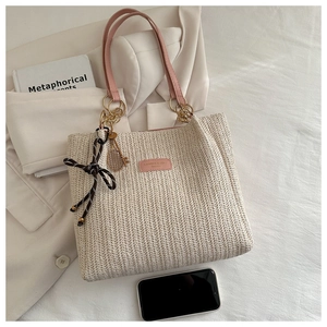 Detail of woven straw tote bag featuring pink leather straps and polka dot ribbon