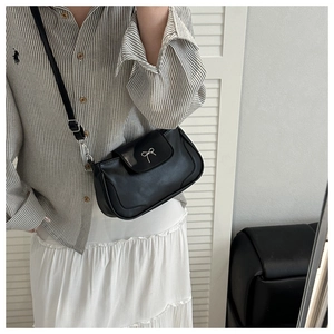 Detail of black rectangular crossbody bag featuring a silver metal bow clasp on a model