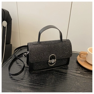 Detail shot of black sequin flap handbag with silver oval lock on a dark wood table