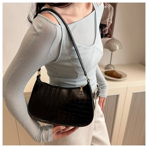 Detail of black crocodile texture baguette bag with golden zipper on a female shoulder