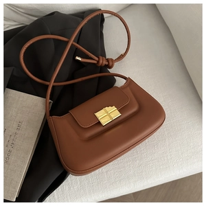 Detailed macro view of caramel brown leather baguette bag with a gold cross-shaped clasp
