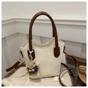 Close-up of cream white bucket bag with wave opening and cute brown monster pendant charm
