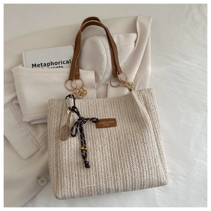 Detail of woven straw tote bag with brown leather handles and decorative metal tennis racket charm