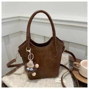 Detail of a dark brown bucket bag with a cute plush charm on a cozy winter table