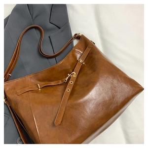 Close-up of vintage brown leather tote bag with gold buckle on a grey blazer