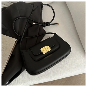 Detailed view of black minimalist handbag with golden square lock and slim knotted strap