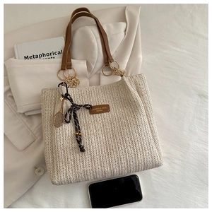 Detail of woven straw tote bag with brown leather straps and metallic tennis racket charm