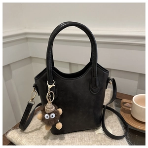 Detail of black vintage bucket bag with plush charm on a cozy knit blanket background