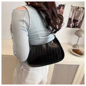 Detail view of black crocodile pattern shoulder bag on model in a cozy interior