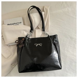 Detail of crinkled patent leather texture and silver bow buckle on black tote bag