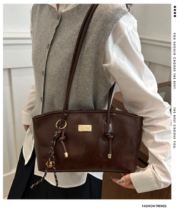Detail view of dark brown leather tote bag with gold metal plaque and knotted strap