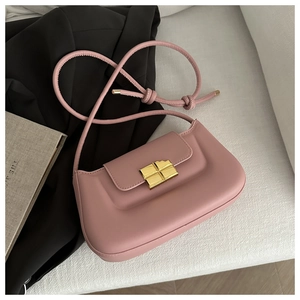 Detailed close-up of pink leather baguette bag with a gold cross-shaped lock on a sofa