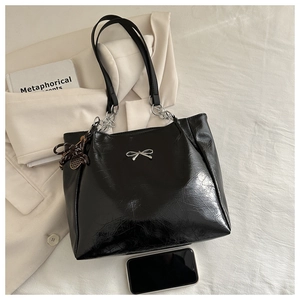 Detail of black glossy tote bag with silver bow accent and chain strap shown with phone