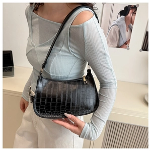Detail of black faux crocodile leather underarm bag worn by model in a chic studio setting