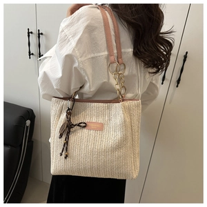 Detail of straw woven tote bag featuring pink leather strap and metallic chain link detail