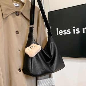Black leather crescent tote bag detail with plush toy charm and canvas shoulder strap