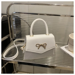 Detailansicht einer weißen Mini-Handtasche mit goldener Schleifenschnalle auf einem Trolley