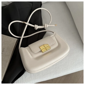 Close-up of cream baguette bag featuring a gold geometric clasp and knotted strap detail