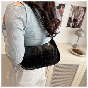 Detail of vintage black crocodile embossed underarm bag on model with gold zipper and leather strap