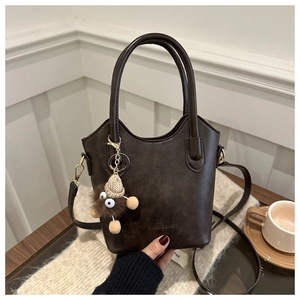 Detail of dark brown vintage bucket bag with plush charm on a wooden table setup