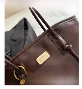 Detailed close-up of dark brown tote bag with gold metal plate and silk scarf accessory