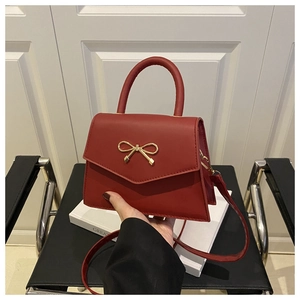 Detailed view of red leather trapezoid handbag with a golden bow metal clasp and top handle
