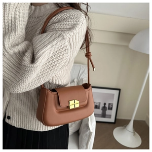 Close-up of caramel brown leather baguette bag with gold buckle in a minimalist setting