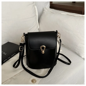 Détail d'un sac seau noir avec boucle dorée et bandoulière sur une literie blanche