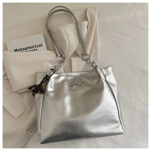 Detail of silver metallic tote bag with bow accent and chain strap on blazer