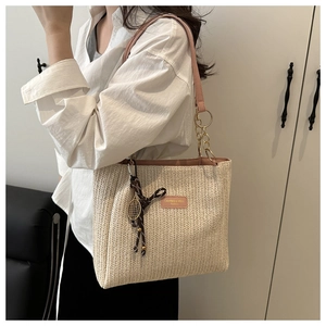 Close-up of woven straw tote bag with pink leather trim and decorative tennis racket charm