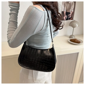 Detail shot of a black crocodile-patterned underarm bag worn on the shoulder by a model