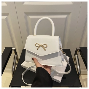 Close-up of a white structured tote bag with a golden bow hardware and a top handle