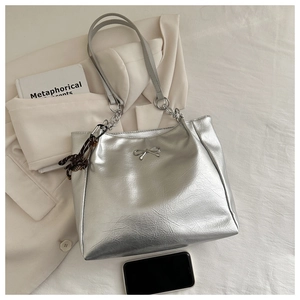 Close-up of metallic silver tote bag with bow detail and chain strap on a blazer
