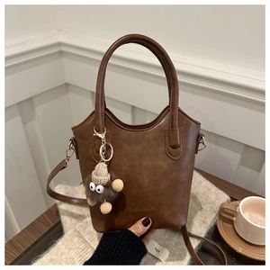 Detail of a brown bucket bag with a plush charm and detachable strap in a cozy setting