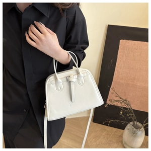 Close-up of a cream bowling handbag featuring buckle details and detachable strap